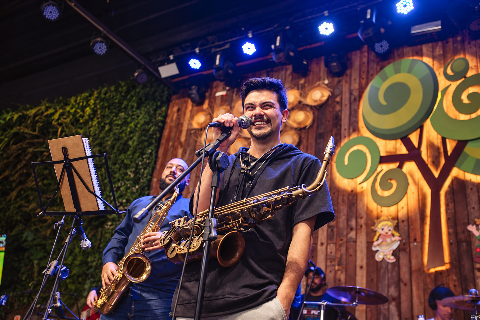 Victor Aguiar a cantar ao microfone com o saxofone dourado, num palco de madeira com banda ao fundo