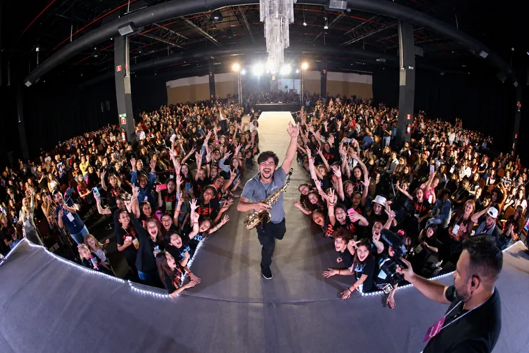 Victor Aguiar a subir a passadeira com o saxofone dourado, saudando uma multidão entusiasta num grande evento em pavilhão